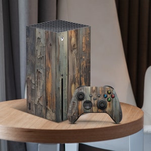 May include: An Xbox Series X console and matching controller with a weathered wood grain design. The console is upright, and the controller is positioned in front. The wood grain has shades of brown, grey, and tan.