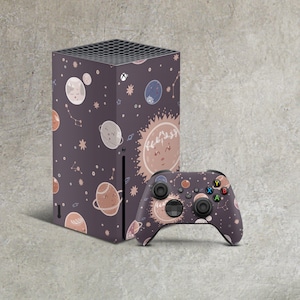 May include: A purple and black video game console with a space-themed design featuring planets, stars, and suns. The console is next to a matching purple and black video game controller.