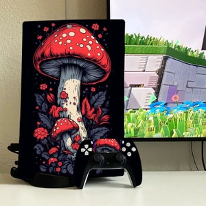 May include: A black gaming console with a custom skin featuring a large red and white mushroom with white spots, surrounded by green leaves and flowers. A black wireless controller is in front of the console.