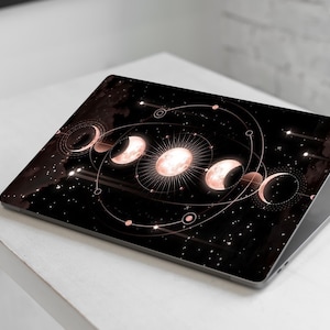 May include: A laptop with a black and rose gold design featuring a celestial pattern of moons and stars. The design is reminiscent of a celestial map.