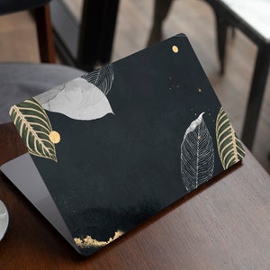 May include: A laptop computer with a black and green leaf design on the lid. The design features gold accents and white leaves.