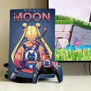 May include: A blue and yellow PlayStation 5 console with a custom skin featuring a cartoon character with blonde hair and a black cat. The skin has the text "セーラームーン MOON" in Japanese and English.