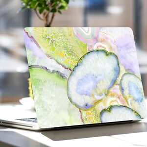 May include: A laptop computer with a colorful abstract design on the back. The design features shades of green, yellow, blue, and purple, resembling agate slices.