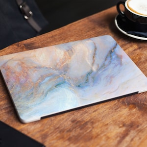 Può includere: Una skin per laptop con un design a marmi blu, bianco e oro. La skin ha una finitura liscia e lucida.