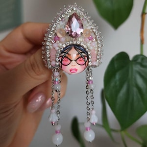 May include: A pink and white beaded brooch with a faceted pink gem and a silver chain with white and pink beads hanging from it.