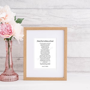 Op de afbeelding: Een ingelijst afdruk met een gedicht met de titel "Thank You for Being a Friend". Het gedicht is gedrukt in zwarte inkt op wit papier. De lijst is van lichtbruin hout met een witte passe-partout. De afdruk ligt op een licht houten oppervlak met roze bloemen in een vaas.
