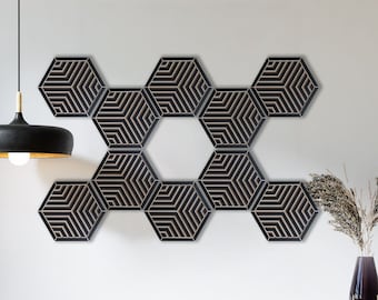 May include: A wall decor made of eight black hexagonal tiles with a geometric pattern. The tiles are arranged in a honeycomb pattern. The decor is hanging on a white wall above a wooden cabinet.