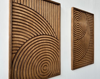 May include: Two wooden wall decor pieces with geometric patterns. The larger piece features a series of concentric circles and vertical lines, while the smaller piece has a more intricate design of overlapping circles.