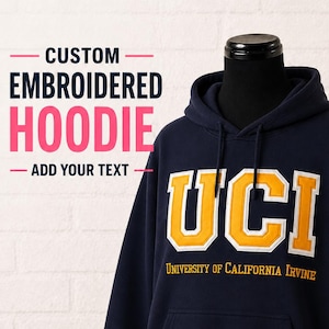 May include: A navy blue hoodie with embroidered yellow and white "UCI" lettering and "University of California Irvine" underneath. The hoodie features a front pocket and hood. The image also includes the text "CUSTOM EMBROIDERED HOODIE - ADD YOUR TEXT".
