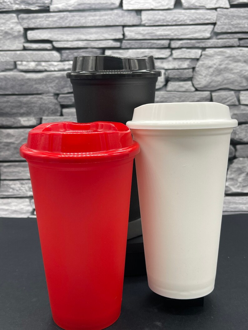 May include: Three reusable coffee cups with lids. One red cup, one black cup, and one white cup. The cups are made of a sturdy material and are designed for hot or cold drinks. The lids are designed to prevent spills.