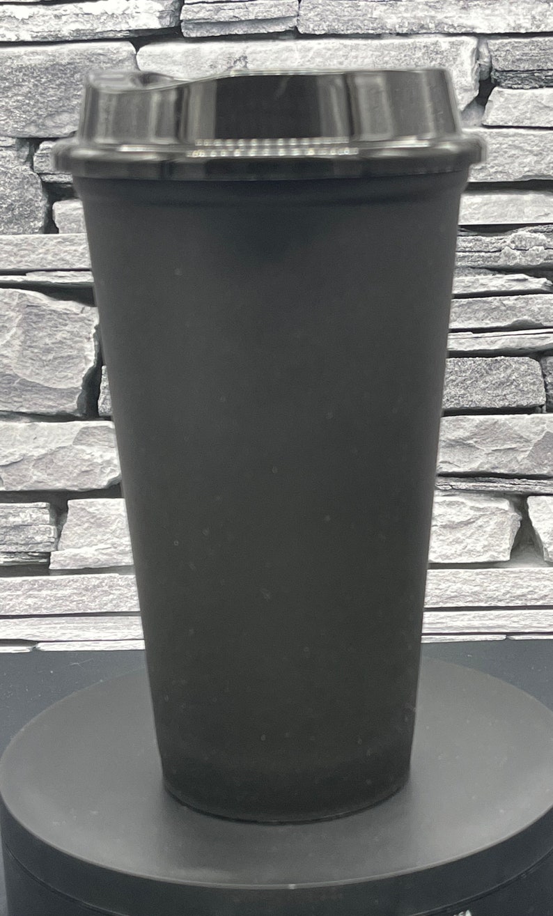 May include: A black travel mug with a black lid. The mug is cylindrical with a slightly tapered design. The lid is a snap-on style. The mug is sitting on a black surface.