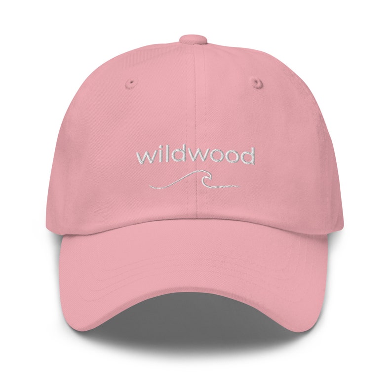 Pu&ograve; includere: Un berretto da baseball rosa con il testo "Wildwood" ricamato in bianco con un piccolo disegno di un'onda sotto.