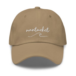 May include: A tan dad hat with white embroidery that says "nantucket" with a wave underneath the text.