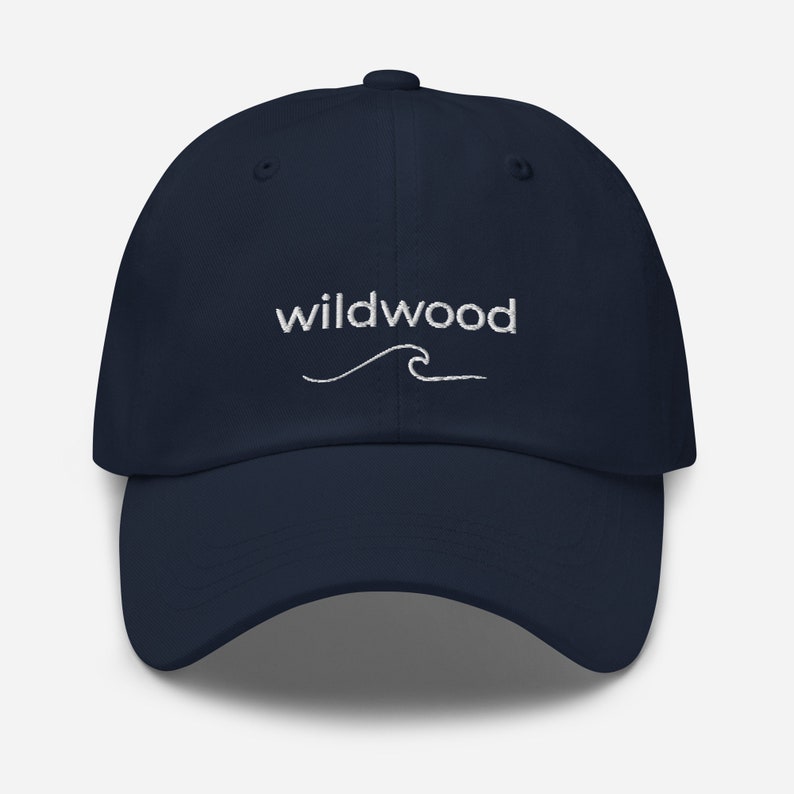 Pu&ograve; includere: Un cappello da baseball blu navy con un'onda ricamata bianca e il testo "wildwood" sopra l'onda.