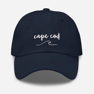 Könnte beinhalten: Eine marineblaue Baseballkappe mit weiß gesticktem Text, der "cape cod" und eine stilisierte Welle zeigt.