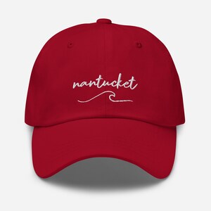 May include: A red baseball cap with white embroidered text that says "nantucket" with a wave underneath.