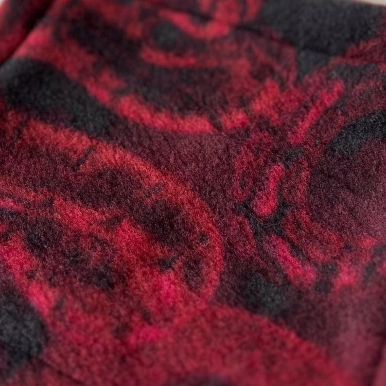 May include: Close-up of a red and black fabric with a marbled pattern. The fabric has a soft, fuzzy texture.