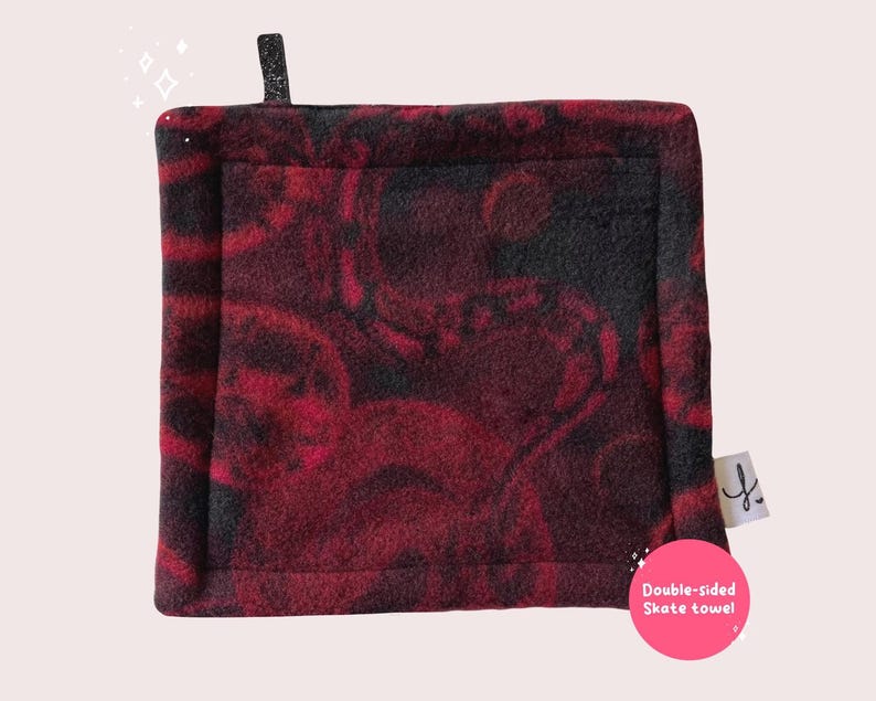 May include: Double-sided skate towel with a red and black marbled pattern. The towel has a black border and a small black tag with a letter 'Y' on it. The text 'Double-sided Skate towel' is written in white on a pink circle.