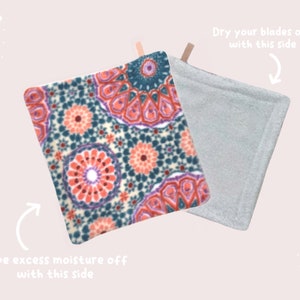 May include: A double-sided cleaning pad with a patterned side and a plain gray side. The patterned side has a colorful mandala design with shades of pink, purple, teal, and white. The text "Dry your blades off with this side" is written above the gray side and "Wipe excess moisture off with this side" is written below the patterned side.