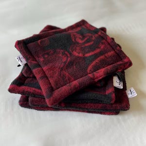 May include: A stack of four red and black fleece pot holders with a floral pattern. Each pot holder has a white tag with a black letter 'f' on it.