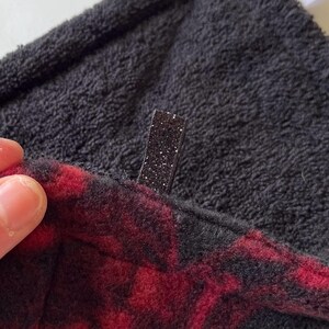 May include: A black fleece fabric with a red and black plaid pattern. The fabric has a black sparkly zipper pull.
