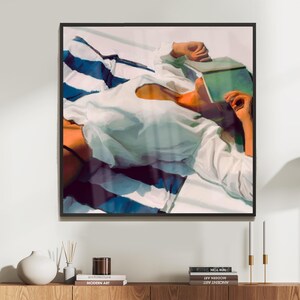 May include: A painting of a person lying on a striped beach towel, wearing a white shirt and holding a book over their face. The painting is done in a realistic style with vibrant colors.