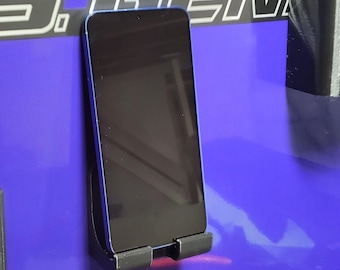 May include: A blue smartphone is mounted on a black holder attached to a purple surface. The surface has the text "RUB" and "J.S. GEM" in white. Other black storage containers hold tools and accessories.