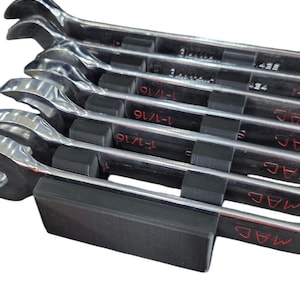 May include: A set of polished metal wrenches, neatly arranged in a black holder. Each wrench is labeled with size markings, including "1-1/16". The wrenches are designed for mechanical work.
