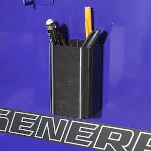 May include: A black pen holder with pens and a pencil attached to a blue surface. The word "GENERAL" is visible in white letters.