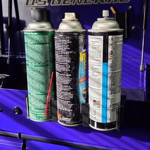 May include: Three aerosol cans in a holder on a blue cabinet. The cans are labeled "Parts Cleaner", "In-Tint", and have warning labels. The cabinet has the text "US GENERAL" on it.