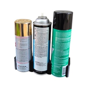 May include: Three spray paint cans in a black holder. The cans are gold, silver, and green with black caps. The gold can is labeled "RUST-OLEUM". The silver can has a warning label. The green can has a black cap.
