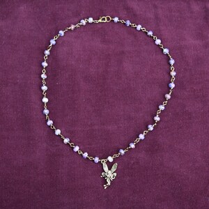 May include: A delicate gold chain necklace with a purple and white bead design. The necklace features a small fairy charm.