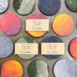 May include: A collection of colorful, round car coasters made of felt. The coasters are in various shades of pink, orange, green, and blue. Each coaster is approximately 4 inches in diameter. Some coasters have a paper band that reads "Maker's Way Fiber Mill Car Coasters."