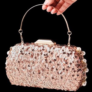 May include: A rose gold sequined clutch with a gold handle and clasp. The rectangular bag is adorned with small, shimmering sequins and pearl accents. The handle is arched, and the bag is set against a black background.