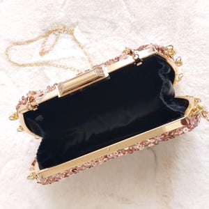 May include: Open rose gold clutch with a gold chain strap. The clutch is covered in sequins and has a gold clasp. The interior is black. A stylish accessory for special occasions.