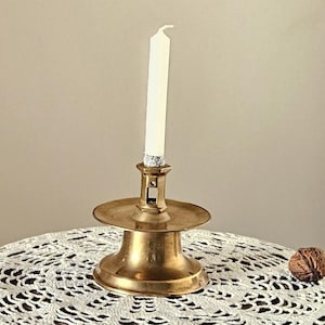 Peut inclure: Petite table en bois vintage avec un bougeoir en laiton et une bougie blanche allumée. Le dessus rond est orné d'un napperon en dentelle blanche. Un socle sculpté et une noix complètent la scène.