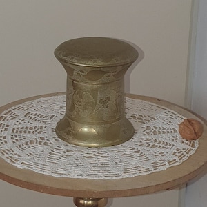 Peut inclure: Un support en métal doré avec un dessus rond et trois pieds. Un récipient en métal doré avec un motif orné se trouve sur le dessus du support.