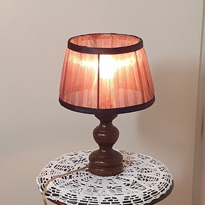 Può includere: Una lampada da terra in legno con una base scolpita e un paralume marrone. La lampada è collegata a una presa di corrente e il cavo è avvolto sul pavimento.