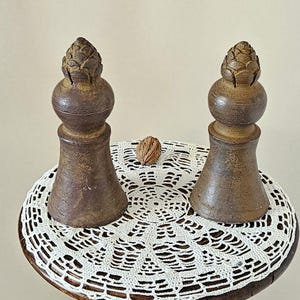 Op de afbeelding: Een antieke, donkerbruine houten bijzettafel met een gebeeldhouwde voet. Het ronde tafelblad heeft een wit kanten kleedje en twee decoratieve houten stukken. Een walnoot ligt op het kleedje. De tafel is ongeveer 76 cm hoog.