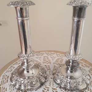 May include: A pair of silver candle holders with ornate designs. The candle holders have a tall, cylindrical base and a wide, flared top.