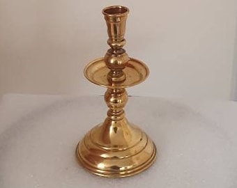 May include: A gold metal candle holder with a round base and a single candle cup. The holder has a decorative design with a raised center section.