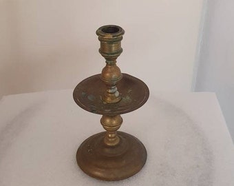 May include: A brass candlestick with a round base and a single candle holder. The candlestick has a worn, aged look.