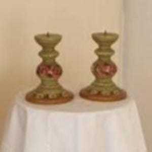 Può includere: Un paio di portacandele in ceramica verde con motivi floreali rosa. I portacandele hanno una base rotonda e un design scanalato.