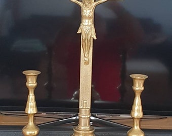 May include: A gold-toned metal crucifix with a figure of Jesus Christ on the cross. The crucifix is on a base with two matching candle holders.