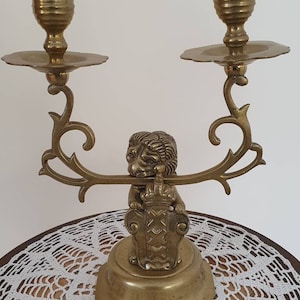 May include: A brass candle holder with two candle cups and a lion figurine holding a shield. The candle holder has a decorative scroll design.