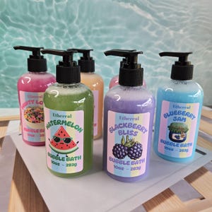 Peut inclure: Cinq flacons à pompe en plastique transparent contenant 283g de bain moussant, aux couleurs distinctes : rose, vert, orange, violet et bleu. Chaque étiquette porte la marque Ethereal, le nom du parfum et une illustration graphique.