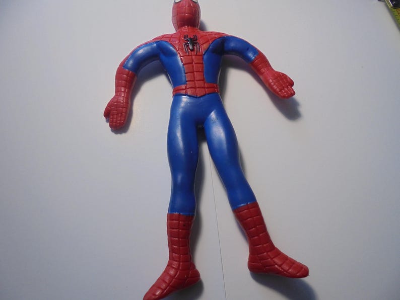 May include: A flexible action figure of a superhero character with a red and blue suit. The figure features a black spider emblem on the chest, a web-like pattern on the red sections of the head, shoulders, and lower legs, and a smooth blue torso.