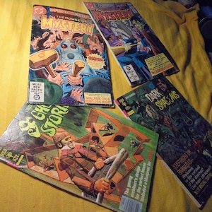 May include: A collection of vintage comic books, including titles like "The House of Mystery", "Mystery", "Dark Shadows", and "Ghost Stories". The covers feature colorful illustrations and text, showcasing classic comic book art.