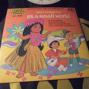 May include: Vintage Walt Disney's "it's a small world" vinyl record album cover. The cover features cartoon illustrations of children in colorful outfits, including a girl in a grass skirt and flower lei. The album includes four songs and is a 33 1/3 RPM record.