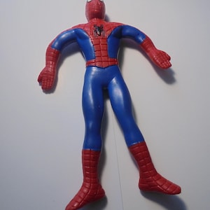May include: A flexible action figure of a superhero character with a red and blue suit. The figure features a black spider emblem on the chest, a web-like pattern on the red sections of the head, shoulders, and lower legs, and a smooth blue torso.
